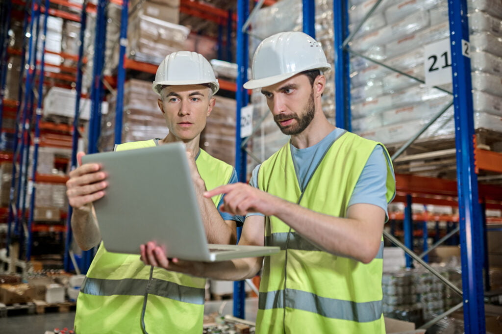 duas pessoas analisando dados em um notebook dentro de uma indústria