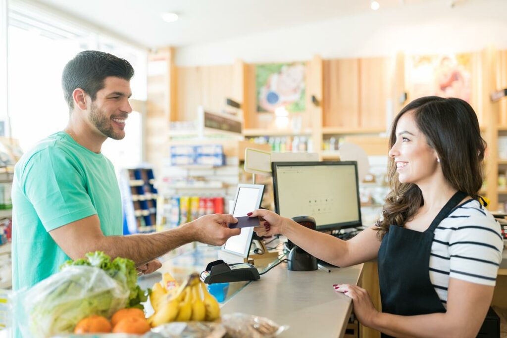 Caixa feminina sorridente com comprador no balcão de check out na mercearia