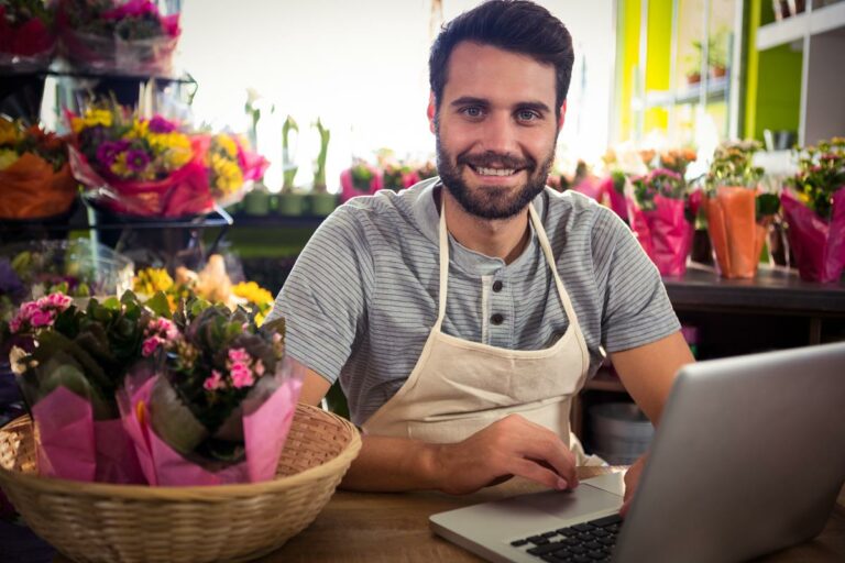 foto de homem em uma floricultura sorrindo trabalhando com seu notebook